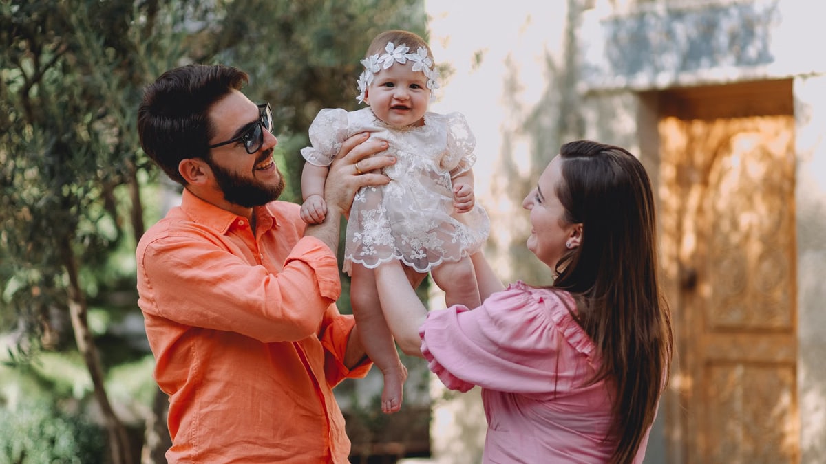 Joyful parents holding their smiling baby girl outside on a sunny day.