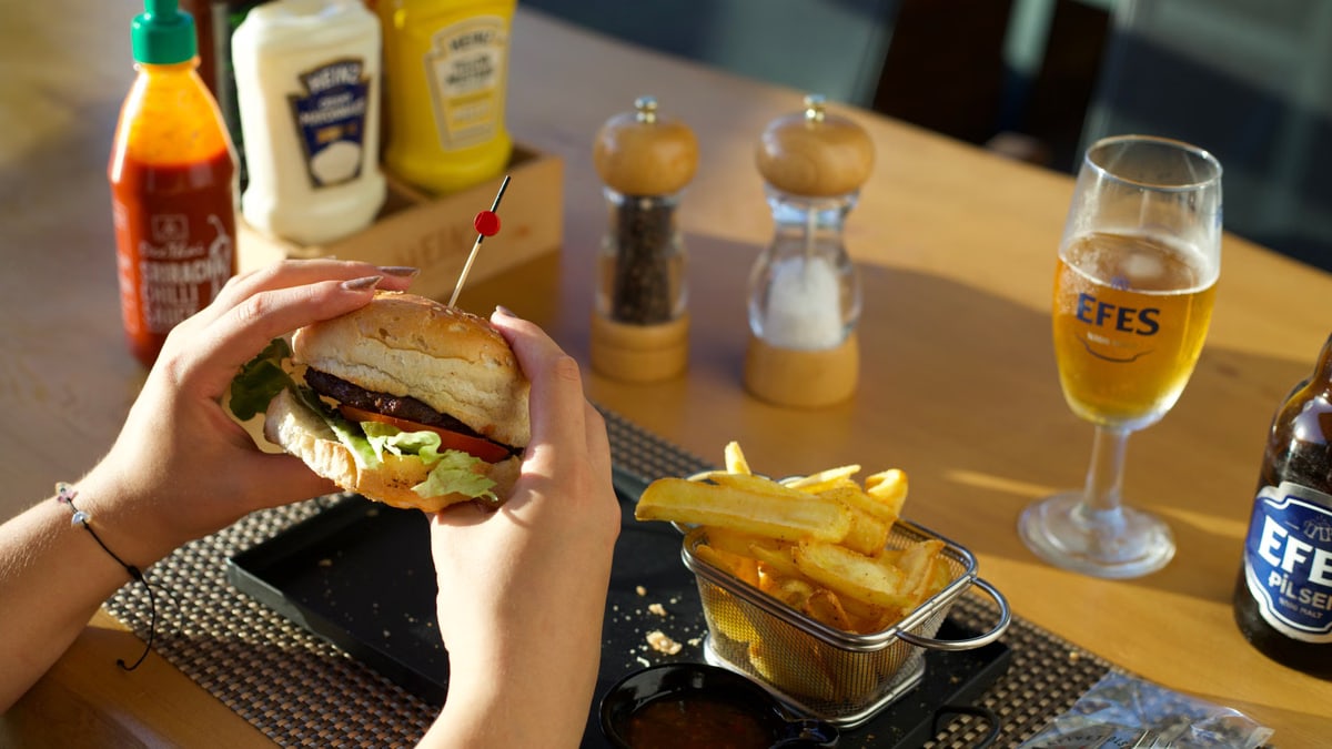 A person enjoying a delicious burger and fries with a glass of beer at a restaurant.